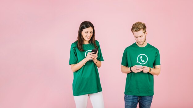 Homme et femme à l&#39;aide de téléphone portable sur fond rose