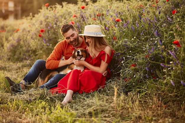 Homme et femme assis avec un drôle Beagle sur le champ vert avec des coquelicots rouges