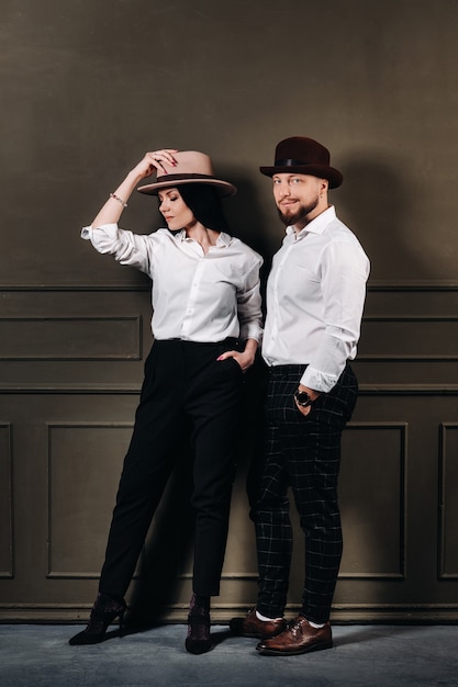 Un Homme Et Une Femme En Chemises Blanches Et Chapeaux Sur Fond Noir. Un Couple Amoureux Pose à L'intérieur Du Studio. Photo Premium