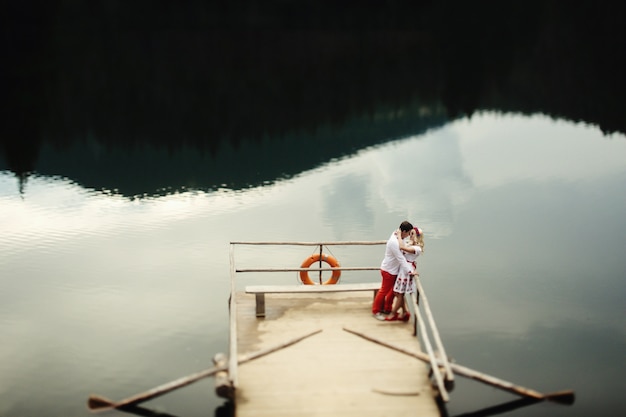 L&#39;homme et la femme embrassent debout sur un porche en bois sur le lac de montagne