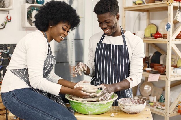 Homme et femme façonnant un pot en argile humide sur roue avec les mains Couple debout à la poterie