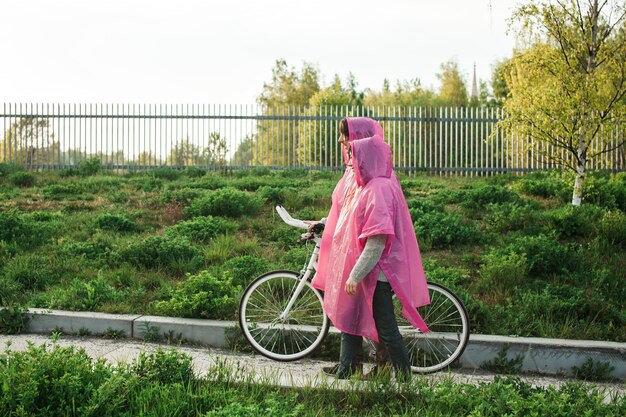 Homme et une femme en imperméable en plastique rose marchant à travers la route avec un vélo à une date