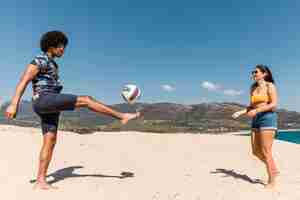 Photo gratuite homme et femme jouant au football sur la plage de sable