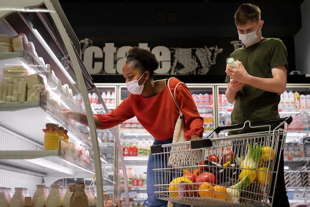 Photo gratuite homme et femme avec des masques médicaux à l'épicerie avec panier