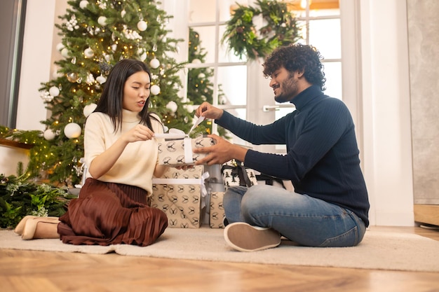 Homme et femme ouvrant une boîte-cadeau assis sur le sol