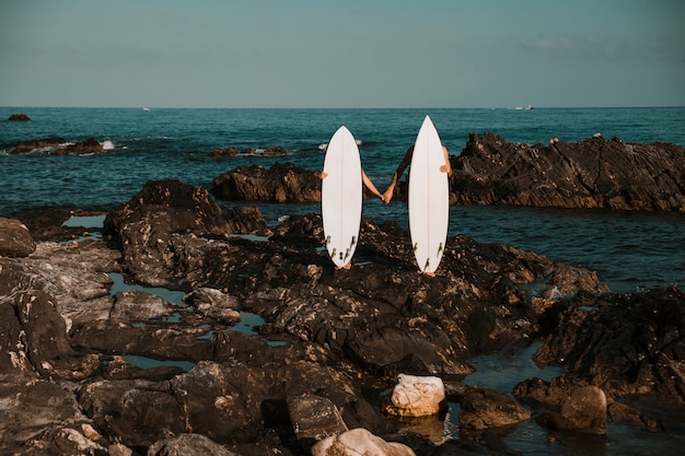 Homme et femme avec des planches de surf, main dans la main sur la côte de Pierre