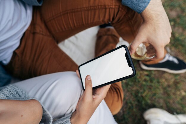 Homme et femme regardant un téléphone tout en ayant un pique-nique à l'extérieur