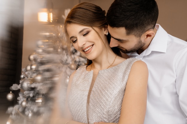 Un homme et une femme en robe argentée s&#39;embrassent devant un arbre de Noël