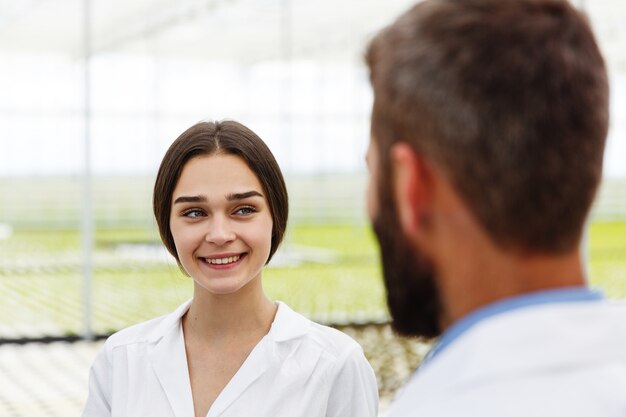 Homme et femme en robes de laboratoire se parlent debout dans la serre