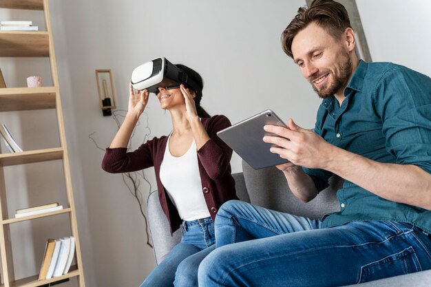 Homme et femme s'amusant à la maison avec un casque de réalité virtuelle et une tablette