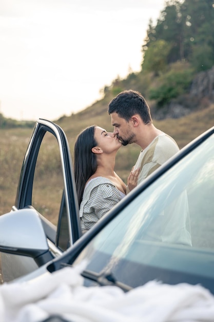 Un homme et une femme s'embrassent dans un champ près d'une voiture.