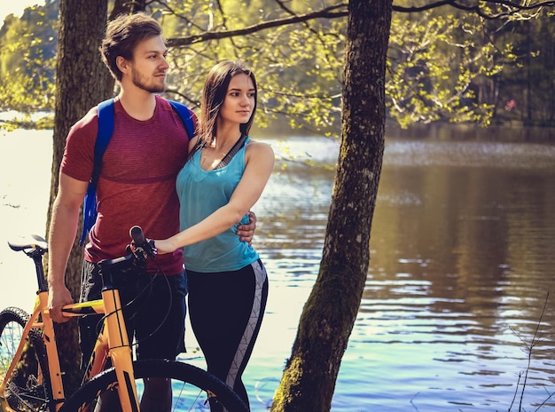 Homme et femme sportifs avec des vélos dans une forêt en journée ensoleillée.