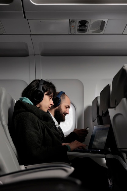 Homme et femme utilisant un ordinateur portable et un smartphone sur un vol en avion, attendant d'arriver en vacances. Couple de passagers travaillant sur des appareils et voyageant avec une compagnie aérienne internationale.