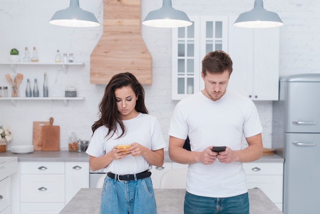 Homme et femme vérifiant les médias sociaux dans la cuisine