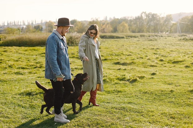 Homme Et Femme En Vêtements De Mode Reposant Sur Une Nature Avec Leur Labrador. Homme Portant Une Veste Et Un Chapeau Noir Et Une Jupe Femme Et Des Bottes Rouges