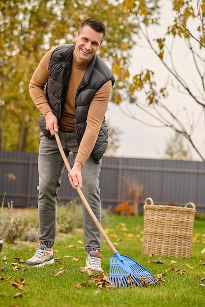 Homme avec des feuilles de nettoyage de râteau regardant la caméra