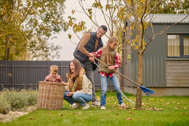 Homme avec fille ratissant des feuilles et femme avec enfant