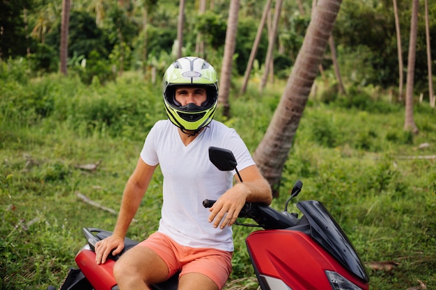 Photo gratuite homme fort sur le champ de la jungle tropicale avec moto rouge