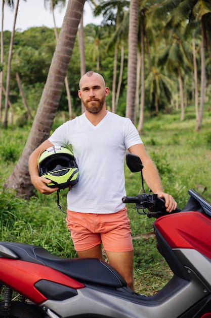 Homme fort sur le champ de la jungle tropicale avec moto rouge