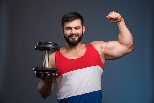 Homme fort montrant des muscles et tenant un haltère.