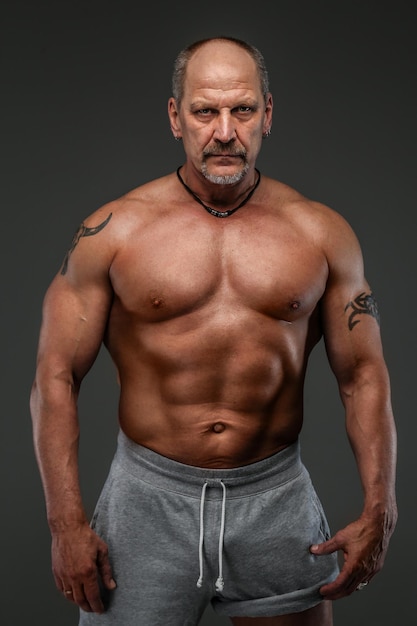 Homme fort et musclé d'âge moyen qui pose en studio. Isolé sur gris.