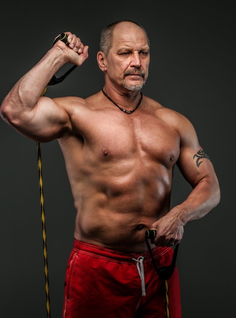 Homme fort et musclé d'âge moyen qui pose en studio. Isolé sur gris.