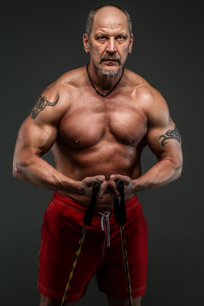 Homme fort et musclé d'âge moyen qui pose en studio. Isolé sur gris.