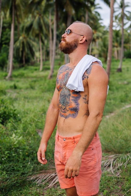 Photo gratuite homme fort tatoué sur champ tropical jungle sans chemise