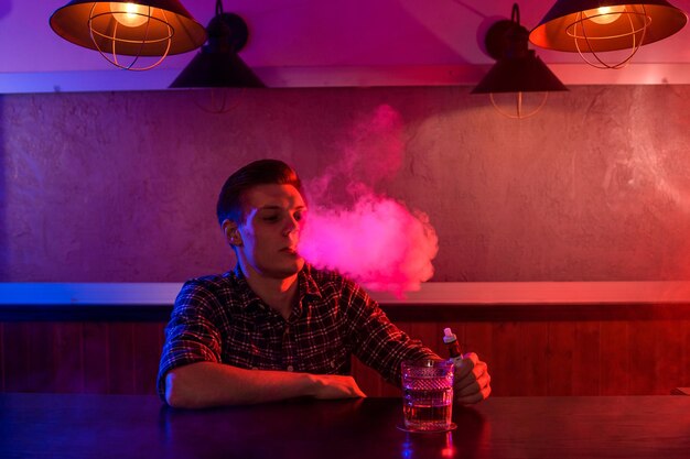 L'homme fume une cigarette électronique au magasin de vapotage. Barre de vapotage.