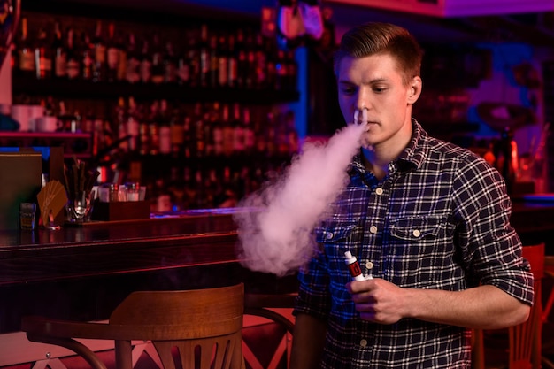 Photo gratuite l'homme fume une cigarette électronique au magasin de vapotage. barre de vapotage.