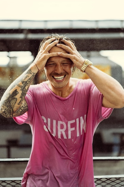 Un homme gai dans un t-shirt brillant avec une planche à roulettes dans un skatepark rit, l'eau éclabousse de ses cheveux.