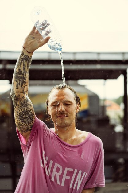 Un homme gai dans un t-shirt lumineux avec une planche à roulettes dans un skatepark verse de l'eau d'une bouteille sur sa tête.