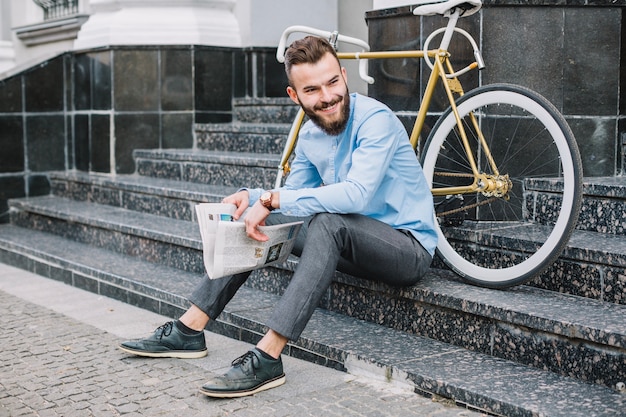 Homme gai avec journal assis sur les escaliers