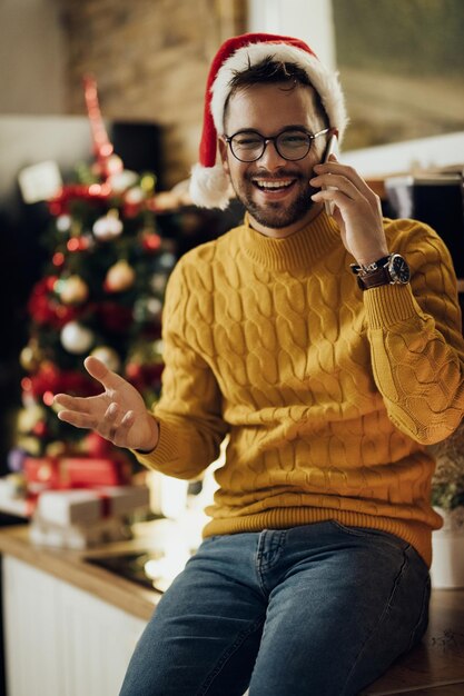 Homme gai parlant au téléphone tout en célébrant Noël à la maison