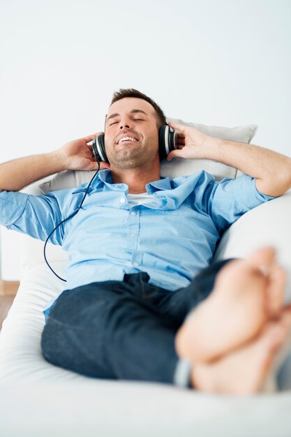 Homme gai portant des écouteurs allongé sur le canapé