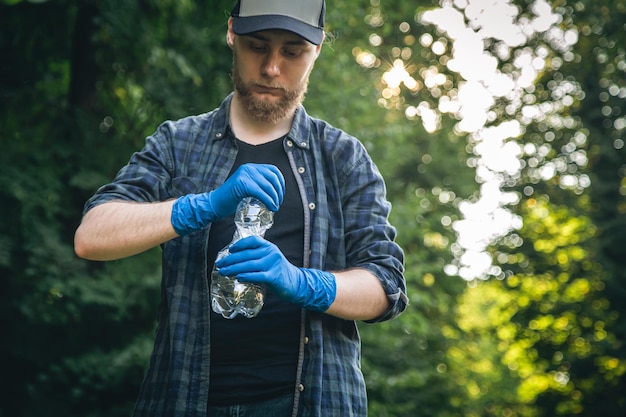 Photo gratuite un homme en gants avec une bouteille en plastique dans ses mains nettoie la forêt