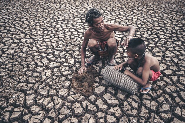 Un homme et un garçon âgés découvrent du poisson sur un sol sec et le réchauffement climatique