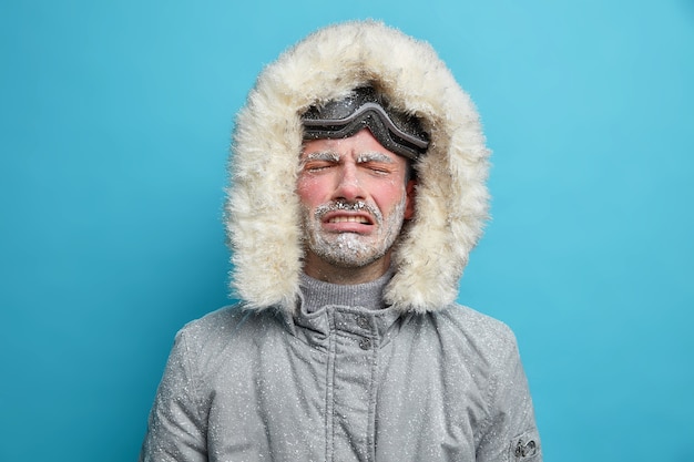 Photo gratuite un homme gelé bouleversé désespéré pleure comme il fait très froid pendant le blizzard et la forte tempête de neige vêtu d'une veste thermo grise avec capuche va skier.