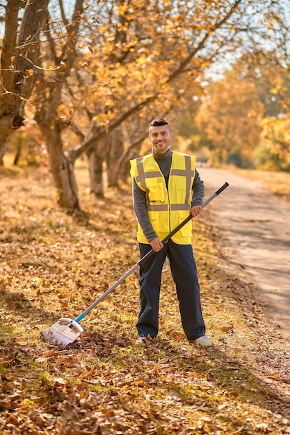 Un homme en gilet jaune ratissant des feuilles dans le parc