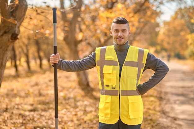 Photo gratuite un homme en gilet jaune ratissant des feuilles dans le parc