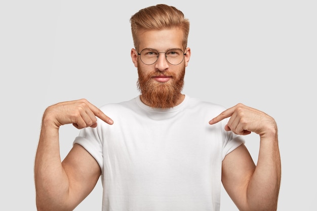 homme gingembre confiant avec coupe de cheveux à la mode, vêtu d'un t-shirt décontracté, indique avec les deux doigts avant