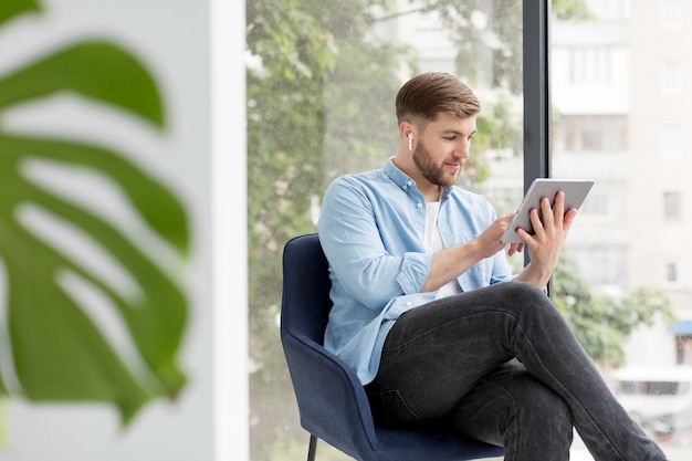 Homme grand angle assis sur une chaise avec tablette