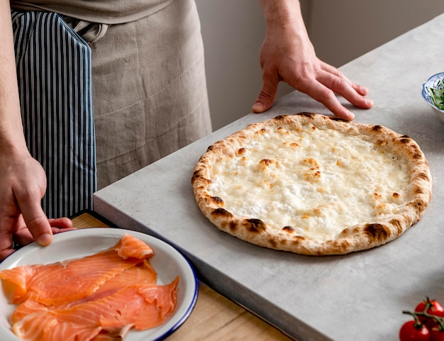 Homme Grand Angle Debout Près De Pâte à Pizza Cuite Au Four Et Tranches De Saumon Fumé
