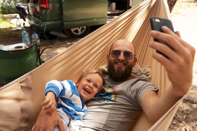 Homme grand angle prenant selfie avec un enfant dans un hamac