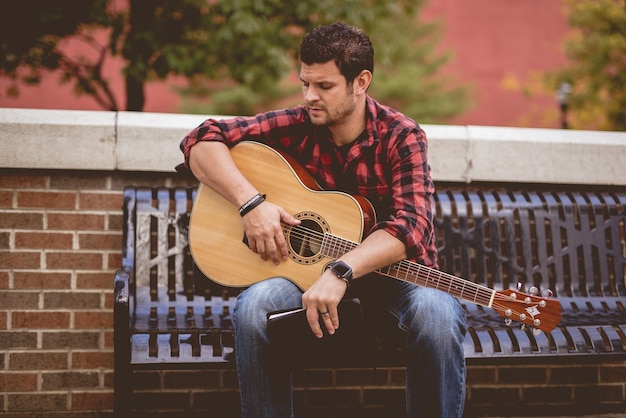 Photo gratuite homme avec une guitare et un livre assis sur un banc dans le parc