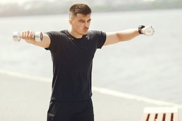 Homme avec des haltères. Guy dans un vêtement de sport. Mâle dans un parc d'été