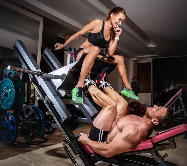 Homme haltérophile faisant des presses à jambes avec son entraîneur. Un couple sportif s'entraîne au gymnase.