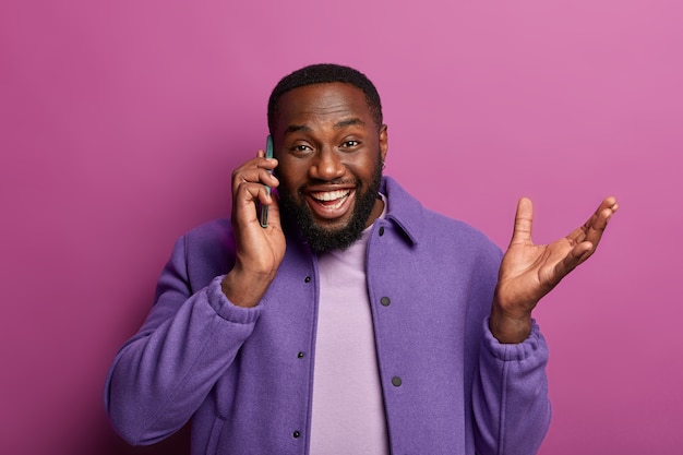 Un homme heureux enthousiaste parle par téléphone portable, reçoit un appel d'un ami ou d'un collègue, discute de bonnes nouvelles, lève la main, raconte quelque chose avec émotion