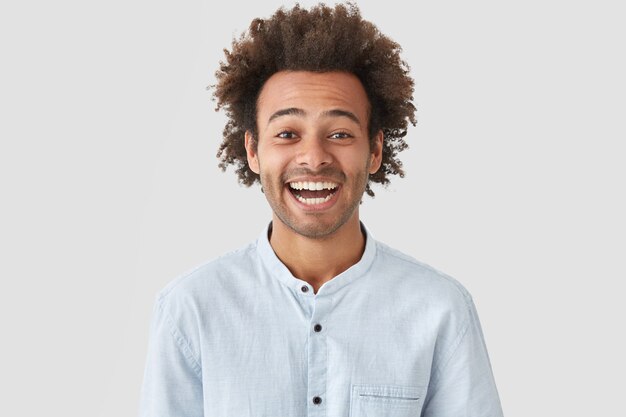 Homme heureux avec une expression joyeuse, a un sourire parfait et des dents blanches, rit de quelque chose de drôle