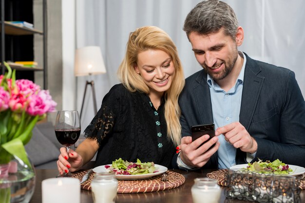 Homme heureux et femme joyeuse à l&#39;aide de smartphone à table
